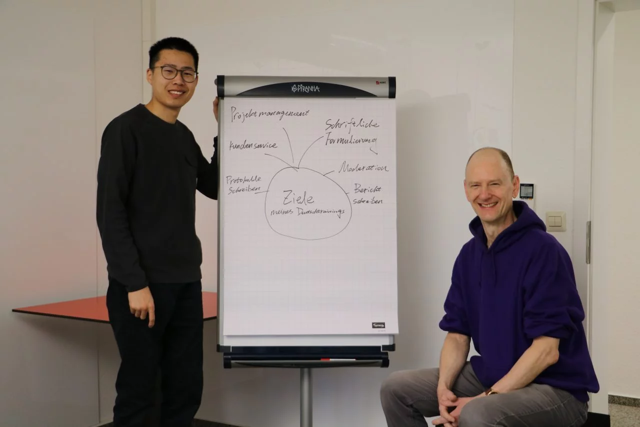 A company employee standing in front of a whiteboard with a line from his German training written on it
